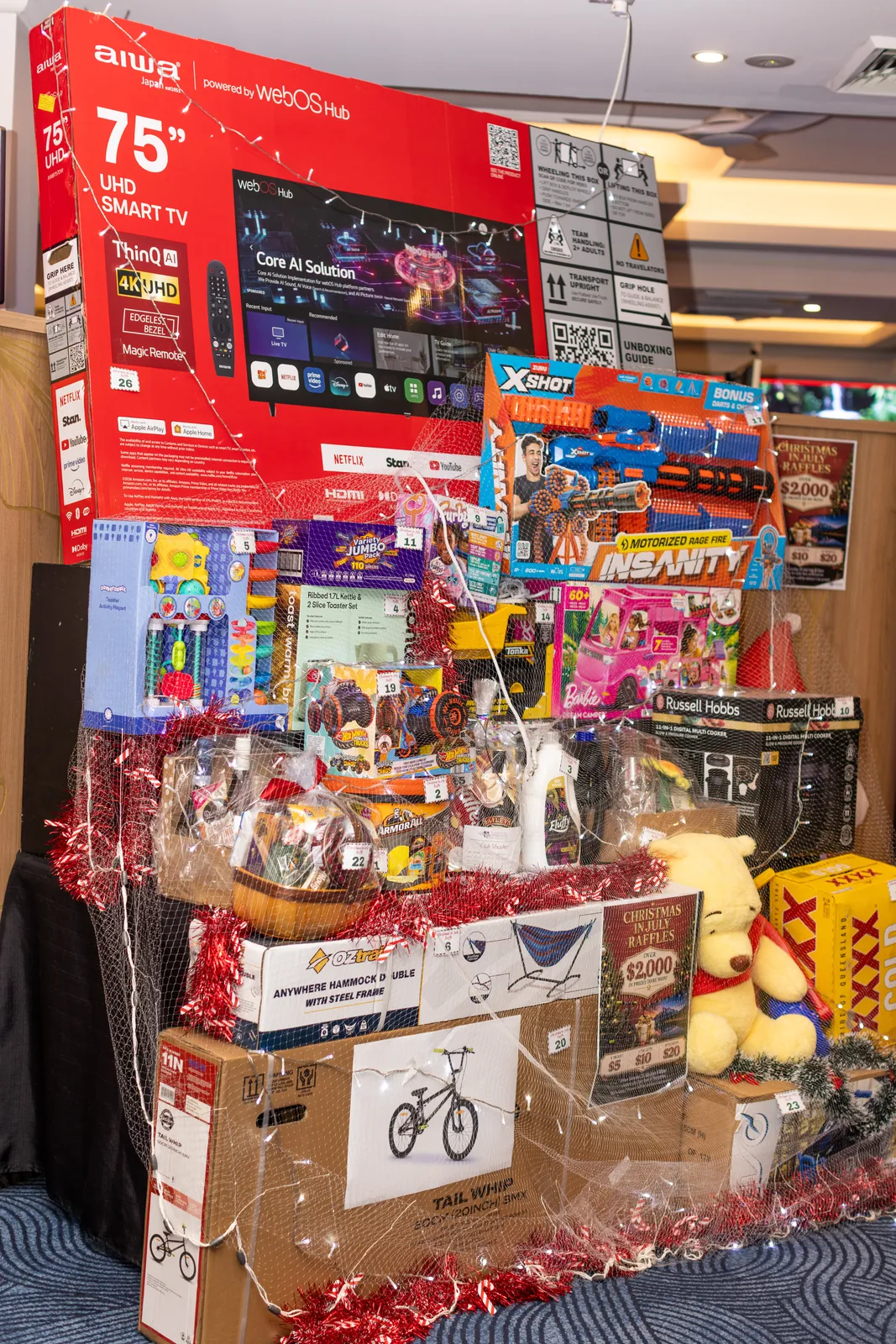 Christmas in July raffle prize display — big-screen TV, kids' bike and hampers